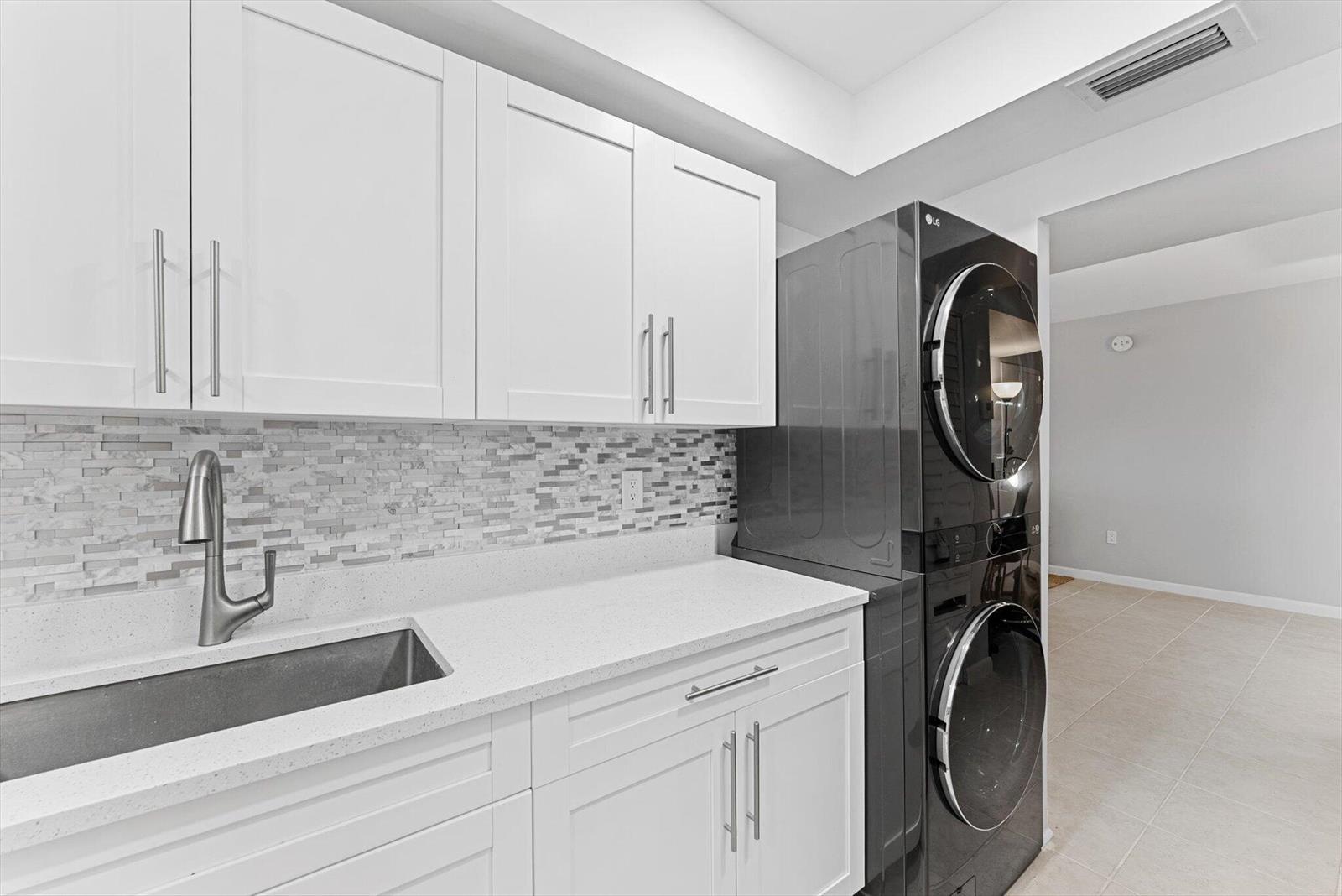 A laundry room features white cabinets, a quartz countertop, a sink, and a stacked washer-dryer — 3450 S Ocean Boulevard # 620, Palm Beach FL 33480, PALM BEACH, FL