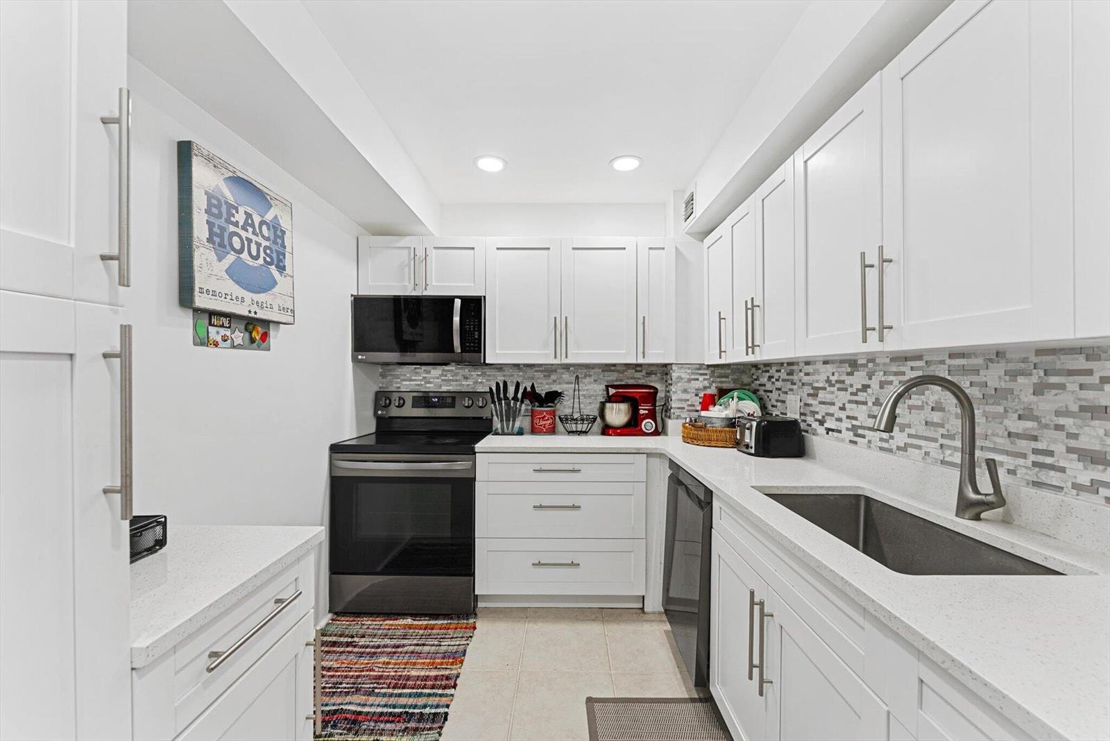 A galley kitchen features white cabinets, stainless steel appliances, and a mosaic tile backsplash — 3450 S Ocean Boulevard # 620, Palm Beach FL 33480, PALM BEACH, FL