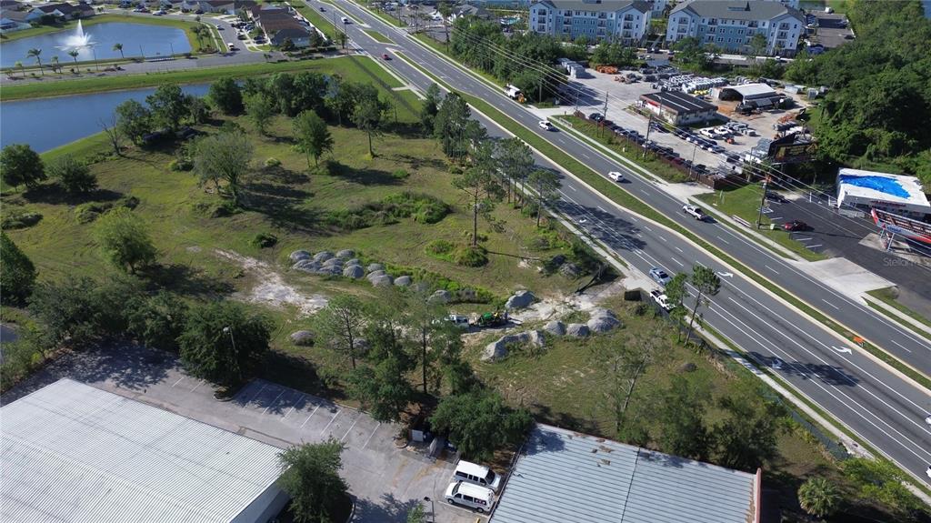 An aerial view shows a vacant, grassy lot situated between a road and commercial buildings — 6347 NARCOOSSEE ROAD, ORLANDO, FL