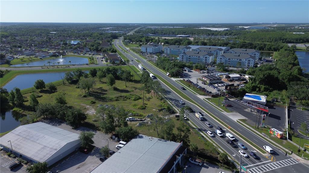 An aerial view shows a multi-lane road, commercial buildings, apartment complexes, and surrounding residential neighborhoods — 6347 NARCOOSSEE ROAD, ORLANDO, FL