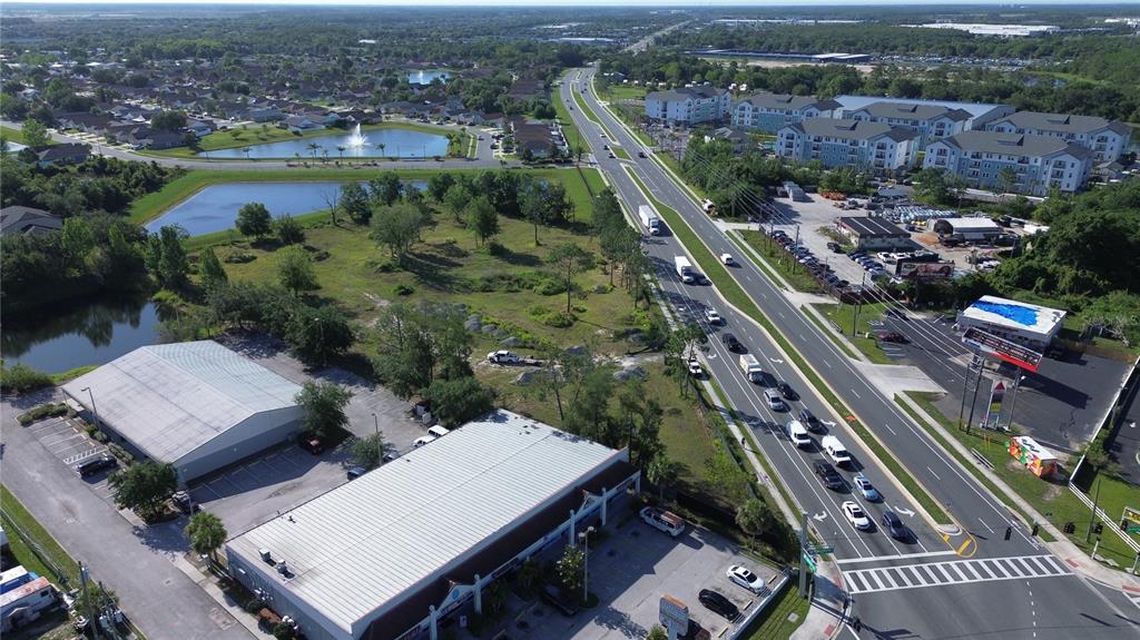 An aerial view shows a commercial area with warehouses, a busy road, and nearby residential apartments — 6347 NARCOOSSEE ROAD, ORLANDO, FL