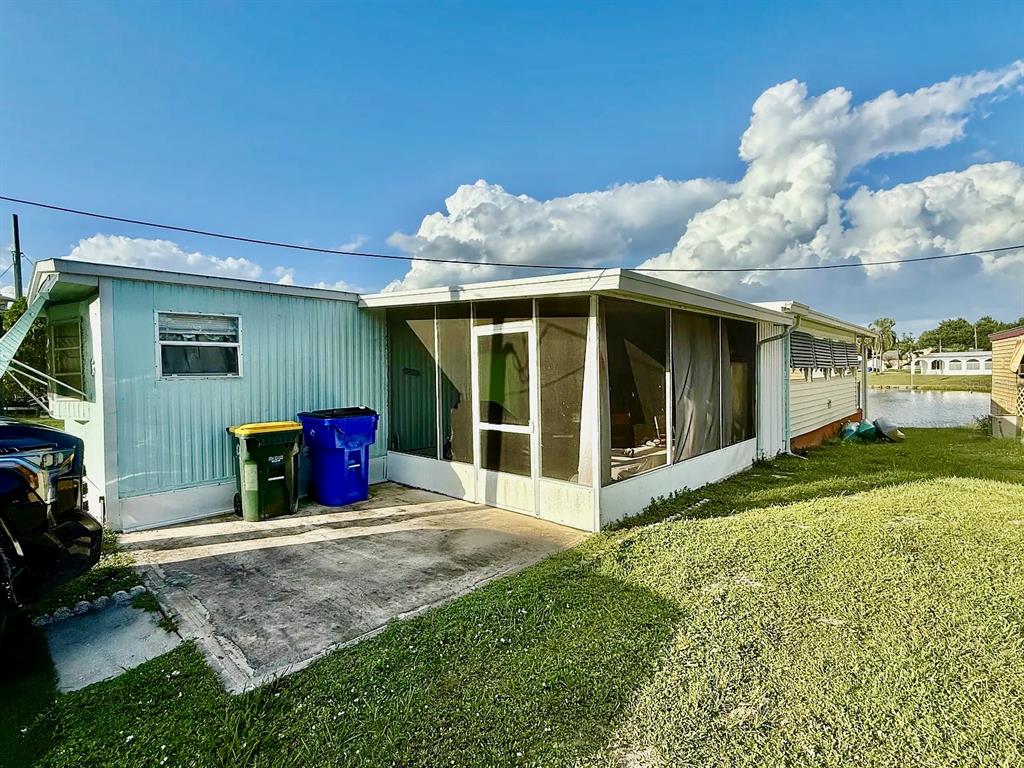 A mobile home with a screened-in porch, concrete patio, and two trash bins outside — 16 W PALM CIRCLE, LAKE PLACID, FL