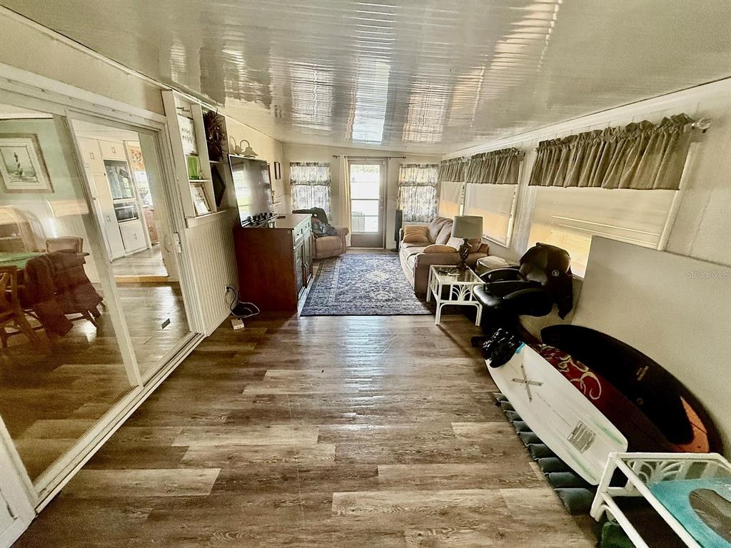 A sunroom with wood-look flooring, a glossy ceiling, and a sliding glass door to the kitchen — 16 W PALM CIRCLE, LAKE PLACID, FL
