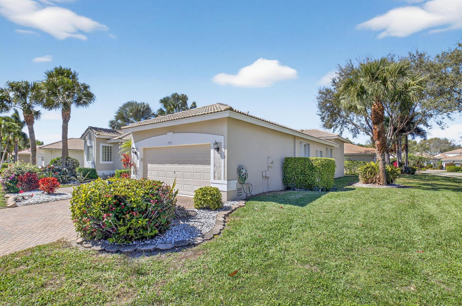 A tan single-story house with a two-car garage, landscaped yard, and palm trees — 7713 Rinehart Drive, Boynton Beach FL 33437, BOYNTON BEACH, FL