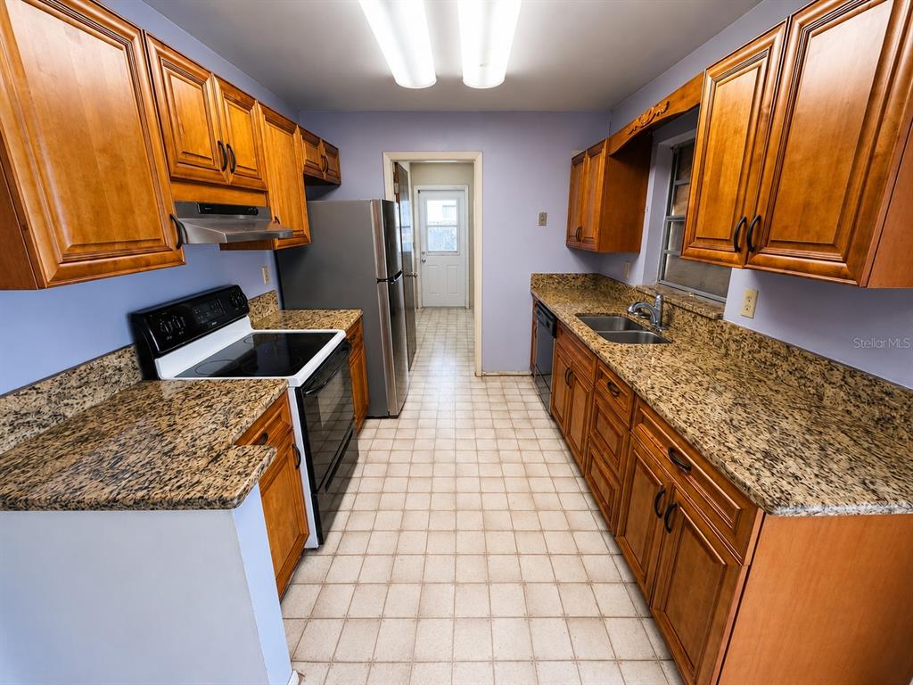 A galley kitchen features wood cabinets, granite countertops, stainless steel appliances, and tile flooring — 539 IMPERIAL AVENUE, MELBOURNE, FL