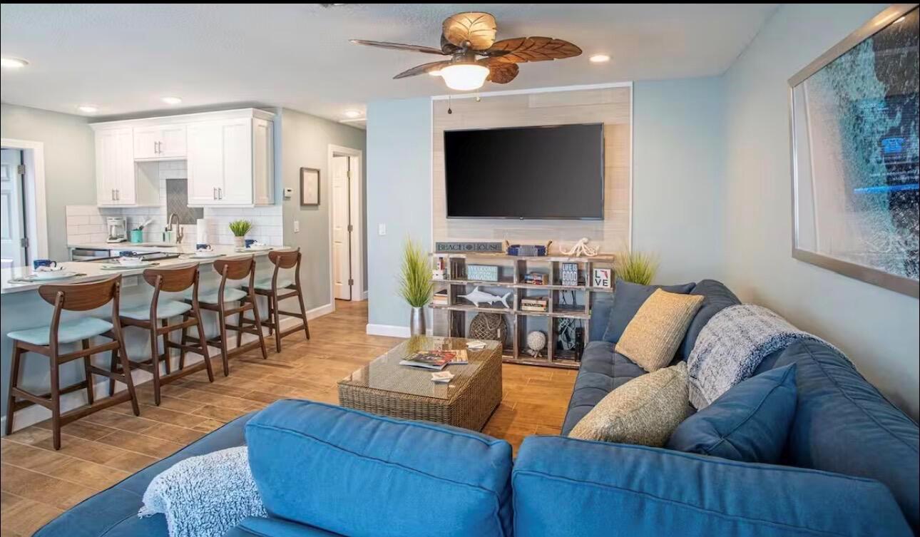 A living room with a blue sectional sofa, a wall-mounted television, and an open kitchen — 85 S Las Olas Drive, Jensen Beach FL 34957, JENSEN BEACH, FL
