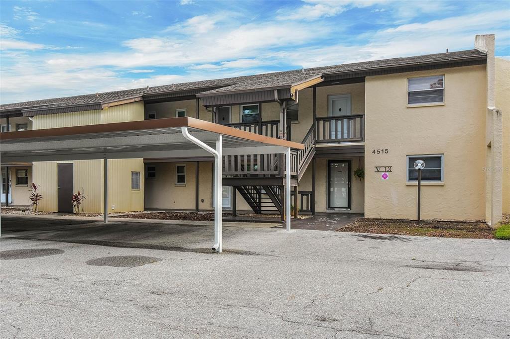 A two-story apartment building exterior features a covered parking area and a wooden staircase — 4515 MARINE PARKWAY UNIT 206, NEW PORT RICHEY, FL