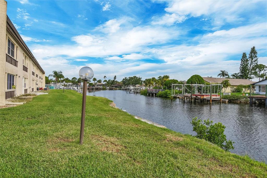 A grassy lawn borders a canal with boat docks alongside a multi-story building — 4515 MARINE PARKWAY UNIT 206, NEW PORT RICHEY, FL
