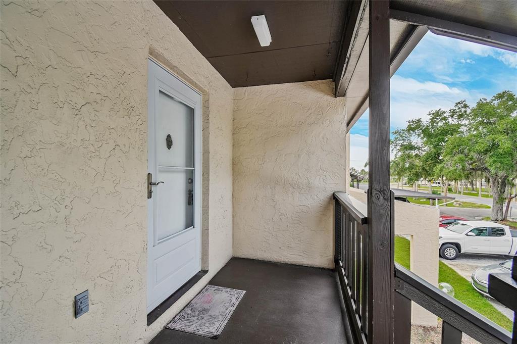 A covered balcony with a white storm door, textured beige walls, and dark wood railings — 4515 MARINE PARKWAY UNIT 206, NEW PORT RICHEY, FL