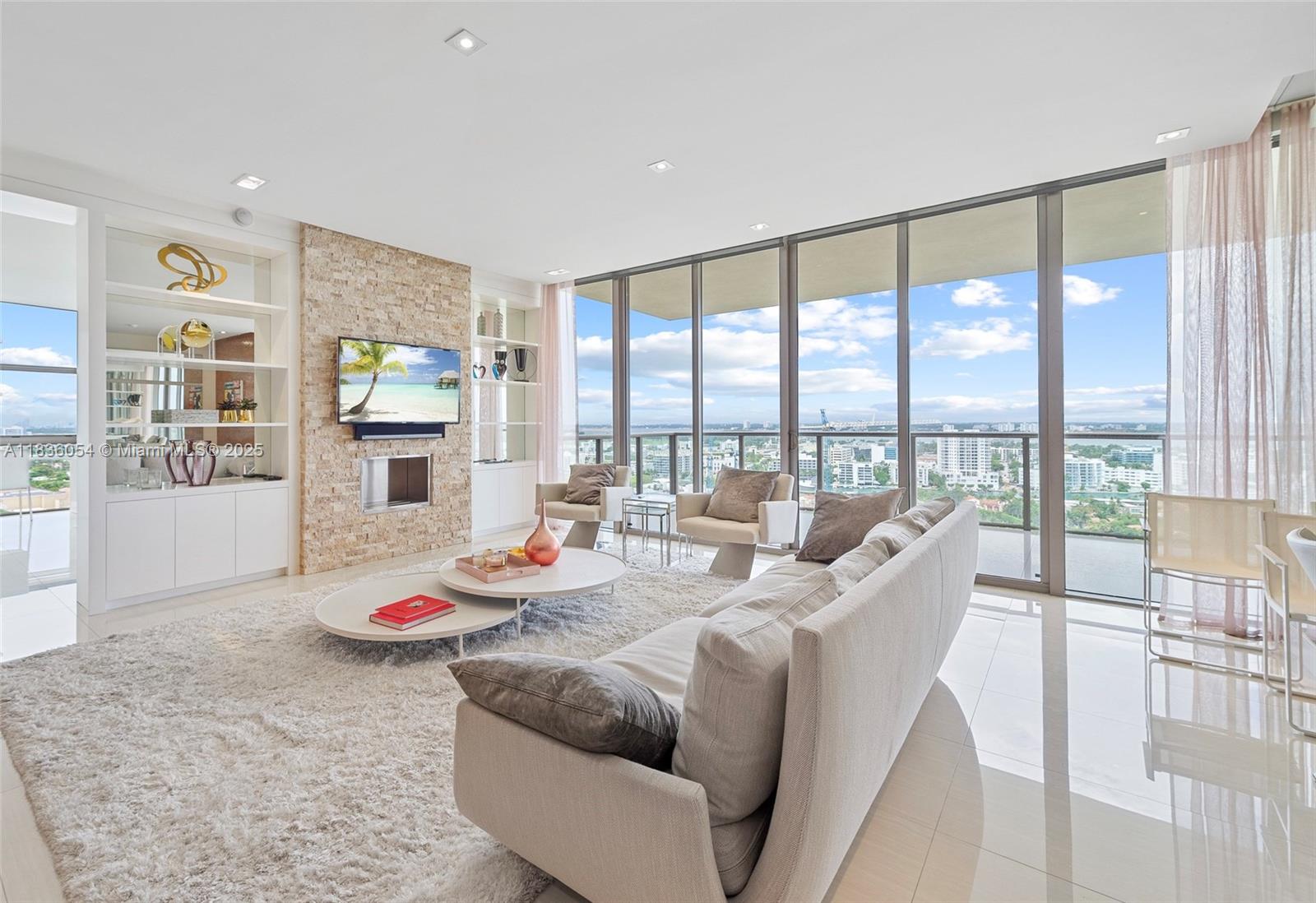 A modern living room features a stone fireplace, white built-in shelving, and floor-to-ceiling windows — 9705 Collins Ave # 1905N, Bal Harbour FL 33154, BAL HARBOUR, FL