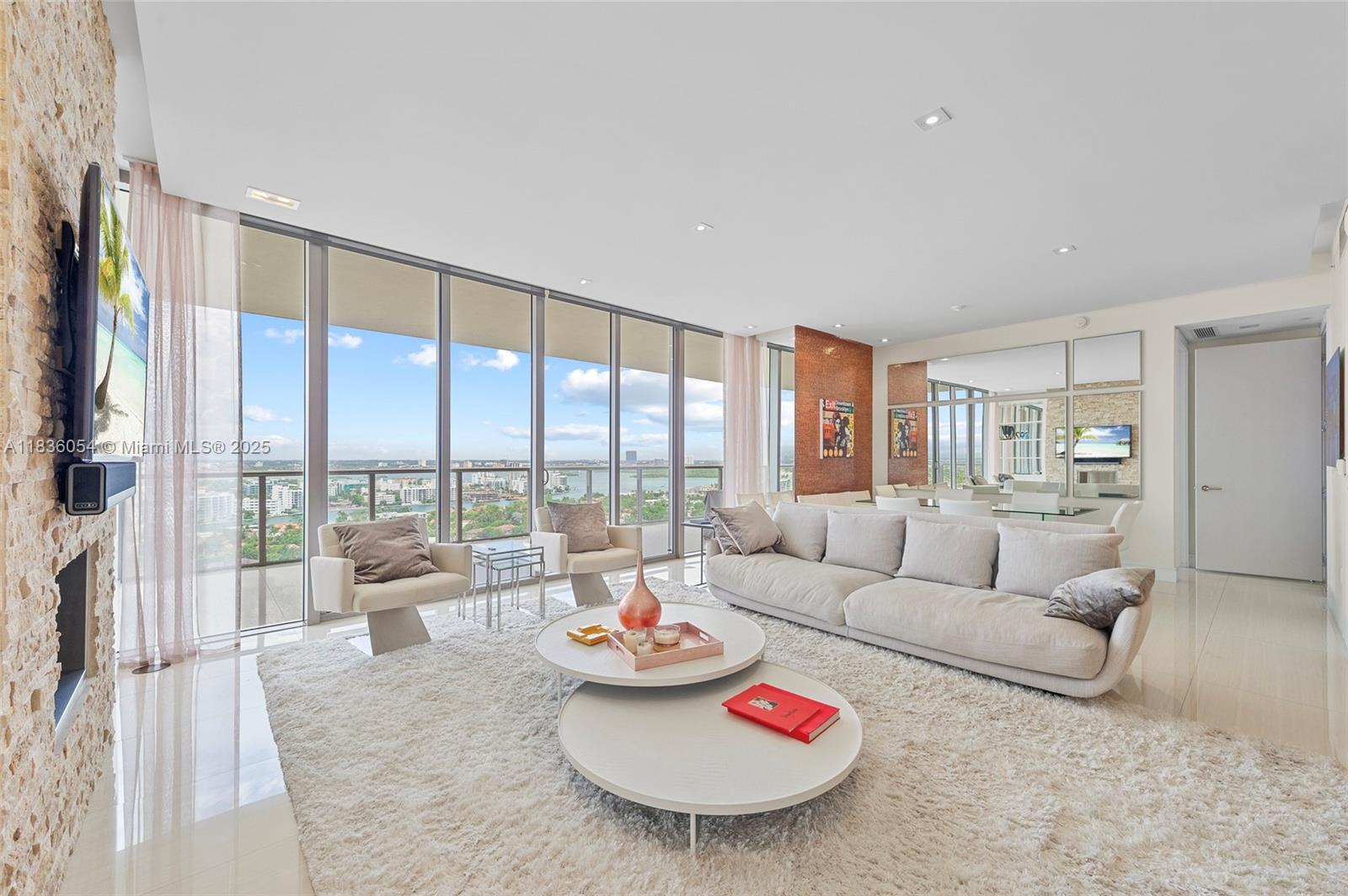 A modern living room features floor-to-ceiling windows, a stone accent wall, and a white rug — 9705 Collins Ave # 1905N, Bal Harbour FL 33154, BAL HARBOUR, FL