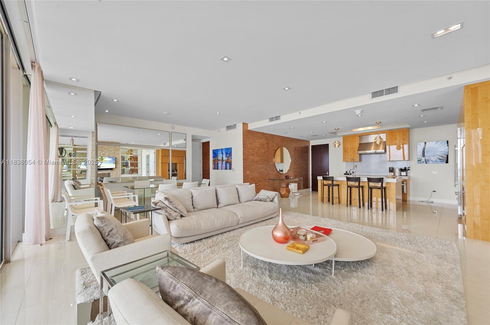 A modern open-concept living room features a white sofa, round coffee tables, and kitchen — 9705 Collins Ave # 1905N, Bal Harbour FL 33154, BAL HARBOUR, FL