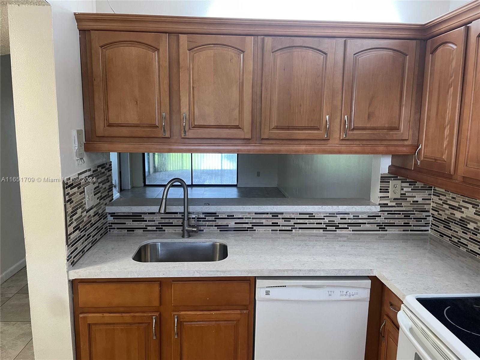 A kitchen features wood cabinets, a stainless steel sink, quartz countertops, and a tiled backsplash — 3252 Foxcroft Rd # 206, Miramar FL 33025, MIRAMAR, FL