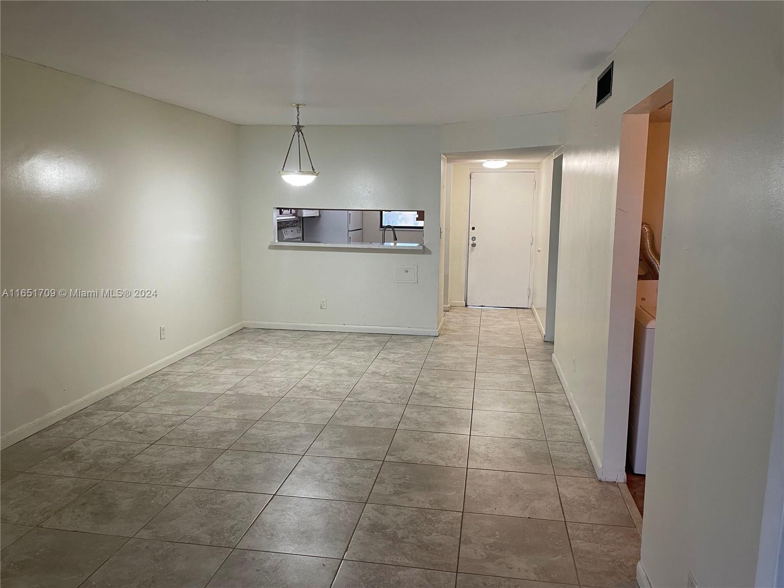 An empty room with light-colored tile flooring features a pass-through window to the kitchen — 3252 Foxcroft Rd # 206, Miramar FL 33025, MIRAMAR, FL