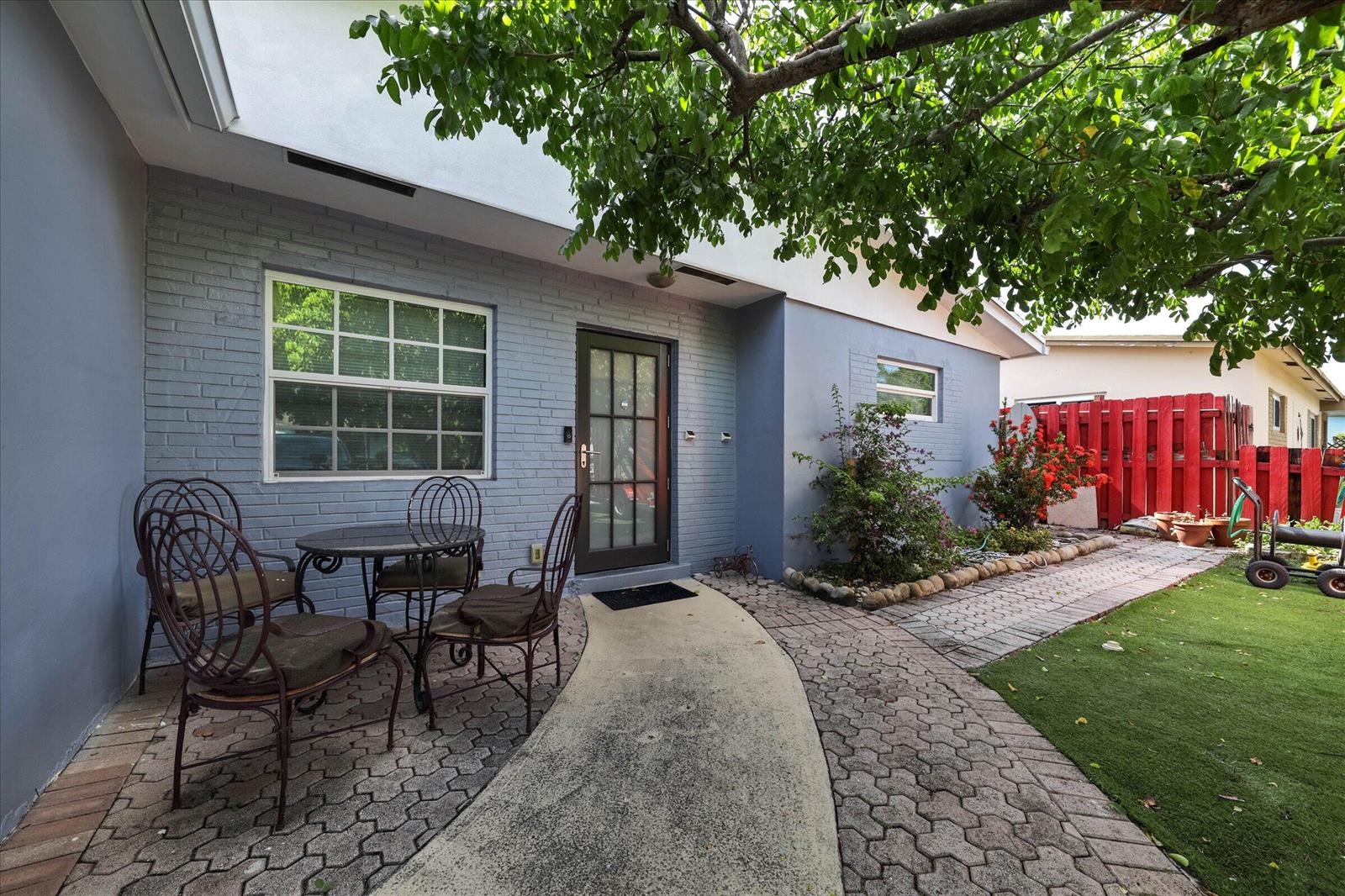 A patio with a table and chairs sits outside a gray brick house with a walkway — 3850 NE 12th Terrace, Pompano Beach FL 33064, POMPANO BEACH, FL