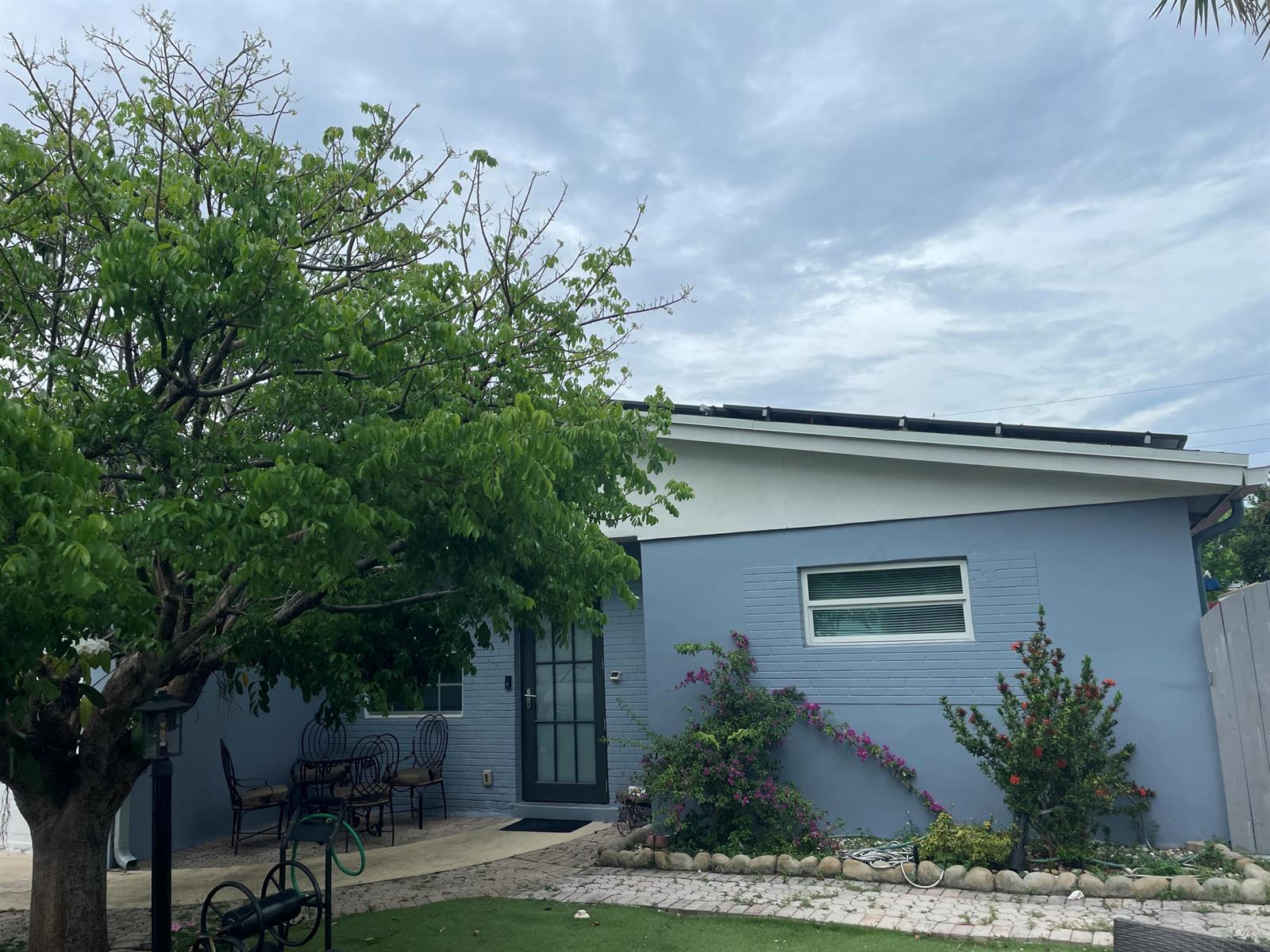 A blue brick house exterior features a front door, a window, and a large tree — 3850 NE 12th Terrace, Pompano Beach FL 33064, POMPANO BEACH, FL