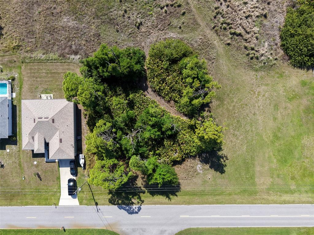 An aerial view shows a house next to a wooded lot along a paved road — 274 SWEETWATER DRIVE, ROTONDA WEST, FL