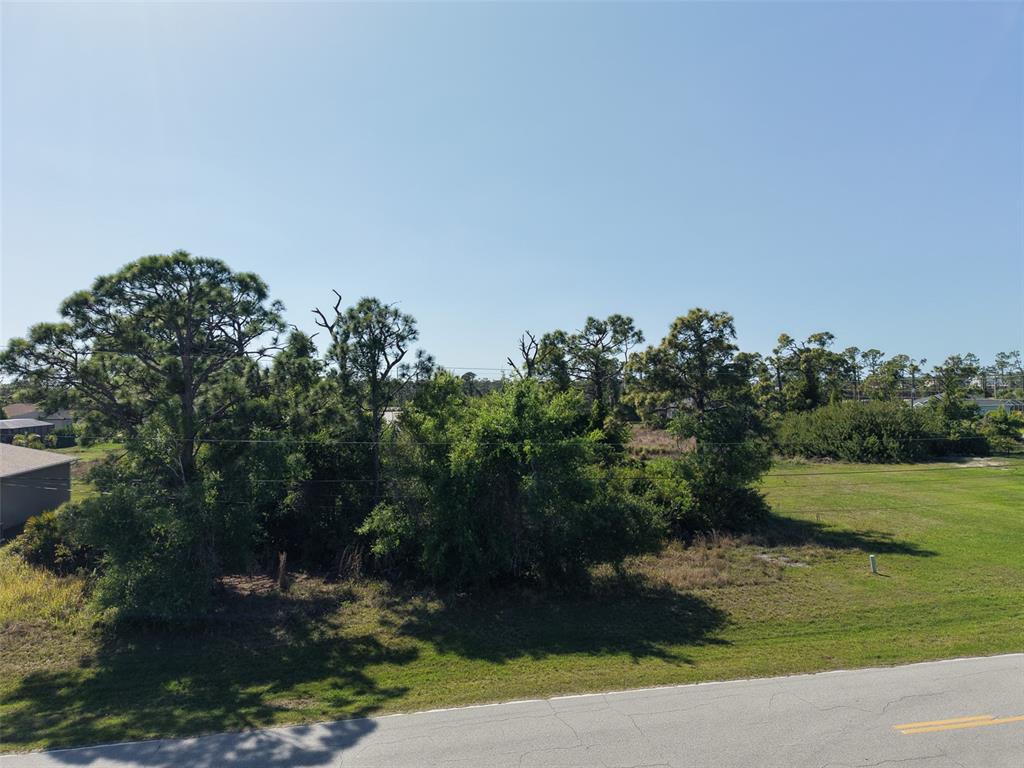 An aerial view shows a grassy, tree-filled vacant lot adjacent to a paved road — 274 SWEETWATER DRIVE, ROTONDA WEST, FL