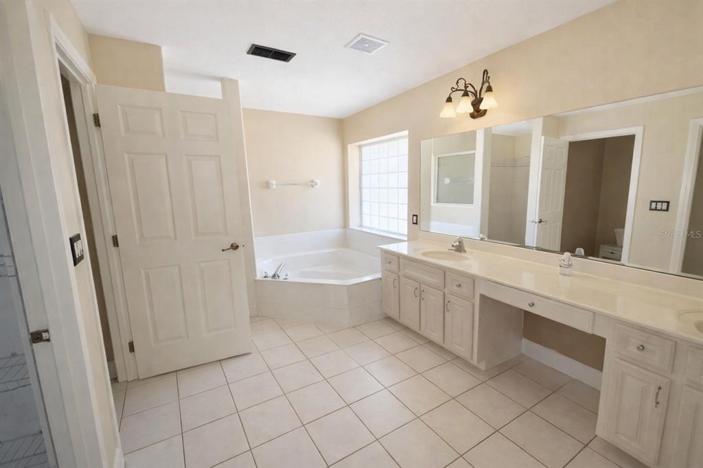 A bathroom features a corner soaking tub, a double vanity with white cabinets, and tile flooring — 791 SE 142 AVENUE, WILLISTON, FL