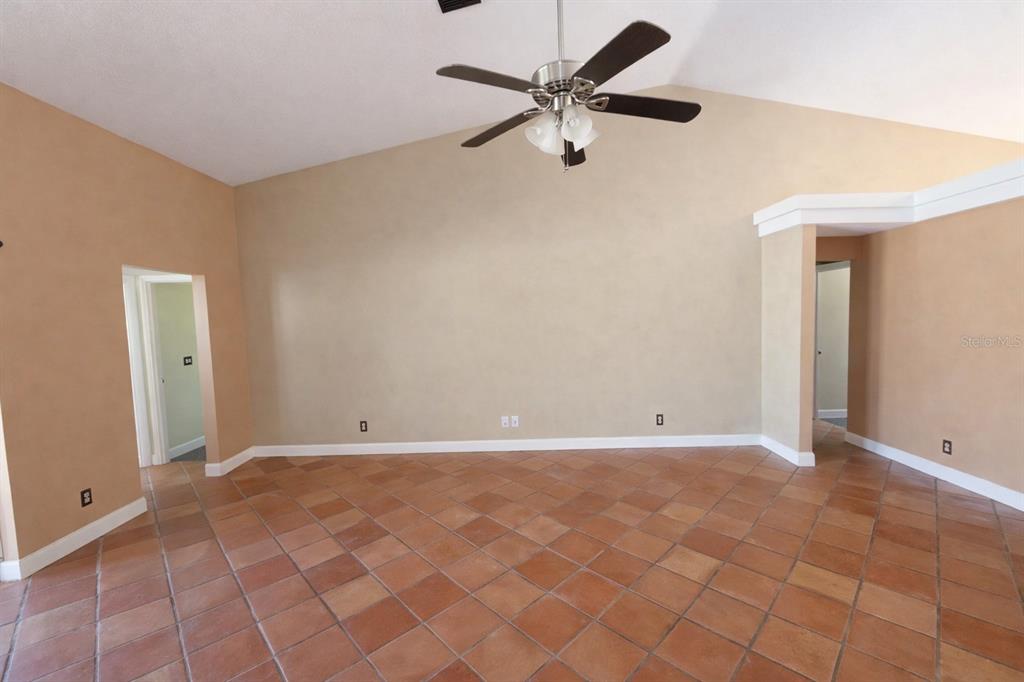 An empty room features terracotta tile flooring, a vaulted ceiling with a fan, and beige walls — 791 SE 142 AVENUE, WILLISTON, FL