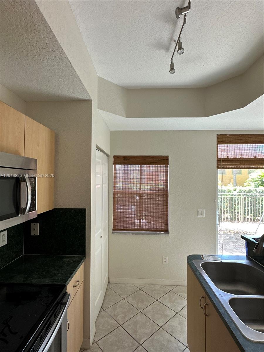 A kitchen features light wood cabinets, dark countertops, tile flooring, and a sliding glass door — 4952 Tradewinds Ter # 506, Dania Beach FL 33312, DANIA BEACH, FL