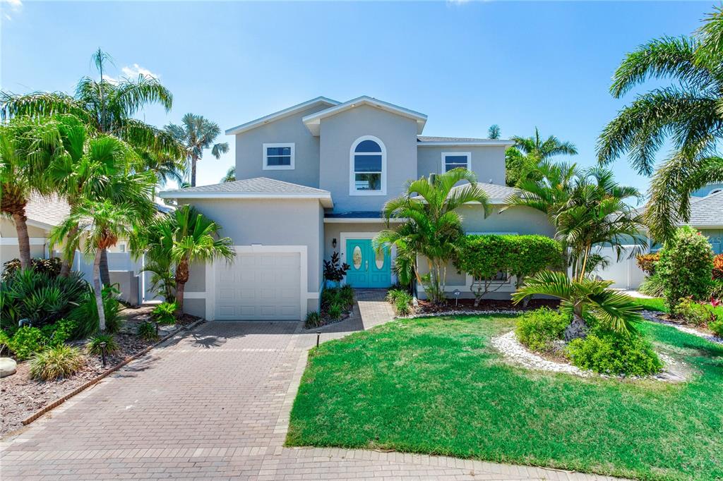 A two-story gray house with a paved driveway, palm trees, and a bright blue front door — 17081 DOLPHIN DRIVE, NORTH REDINGTON BEACH, FL