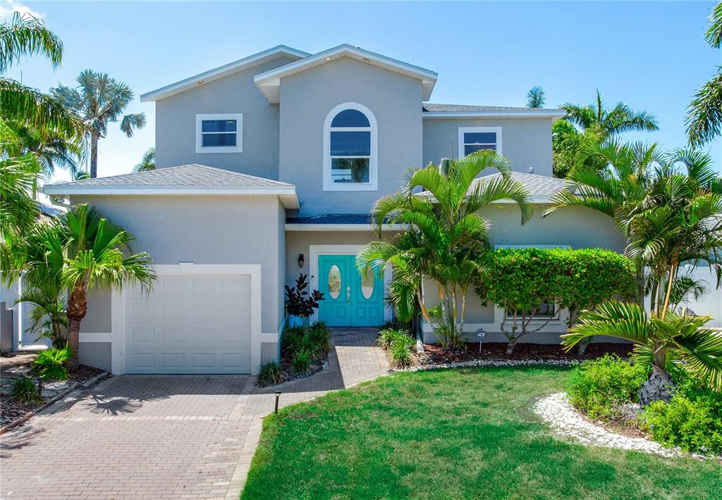 A two-story house with a turquoise front door, a single-car garage, and surrounding palm trees — 17081 DOLPHIN DRIVE, NORTH REDINGTON BEACH, FL