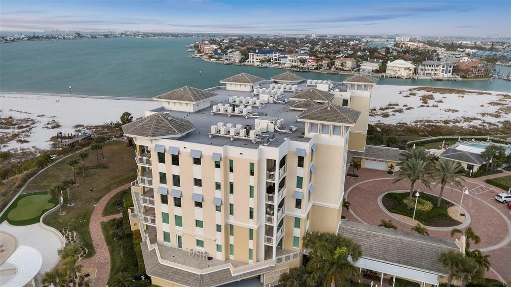 An aerial view shows a multi-story tan building situated on a sandy beach near water — 800 COLLANY ROAD UNIT 302, ST PETERSBURG, FL