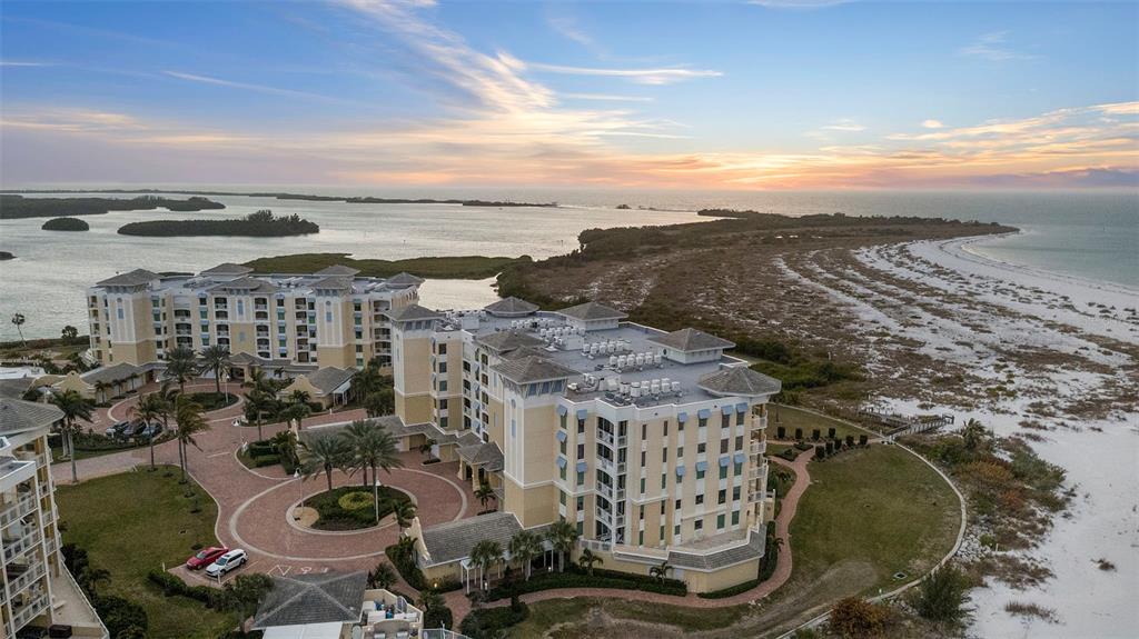 An aerial view shows a multi-story resort building situated on a sandy beach at sunset — 800 COLLANY ROAD UNIT 302, ST PETERSBURG, FL