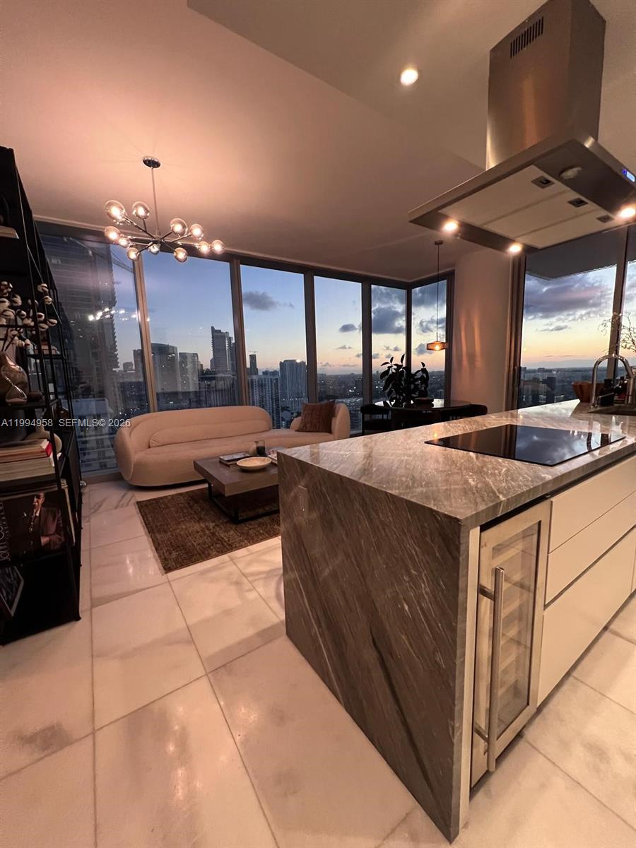 A modern kitchen with a stone island overlooks a living area with floor-to-ceiling windows — 700 NE 26th Ter # 2805, Miami FL 33137, MIAMI, FL