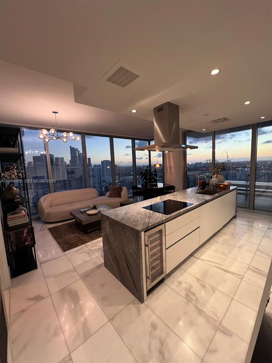 A modern kitchen with a stone island and wine cooler overlooks a living area — 700 NE 26th Ter # 2805, Miami FL 33137, MIAMI, FL