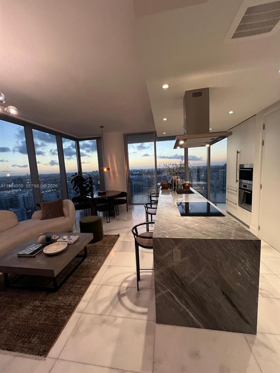 A modern open-concept kitchen and living area features a marble island and floor-to-ceiling windows — 700 NE 26th Ter # 2805, Miami FL 33137, MIAMI, FL