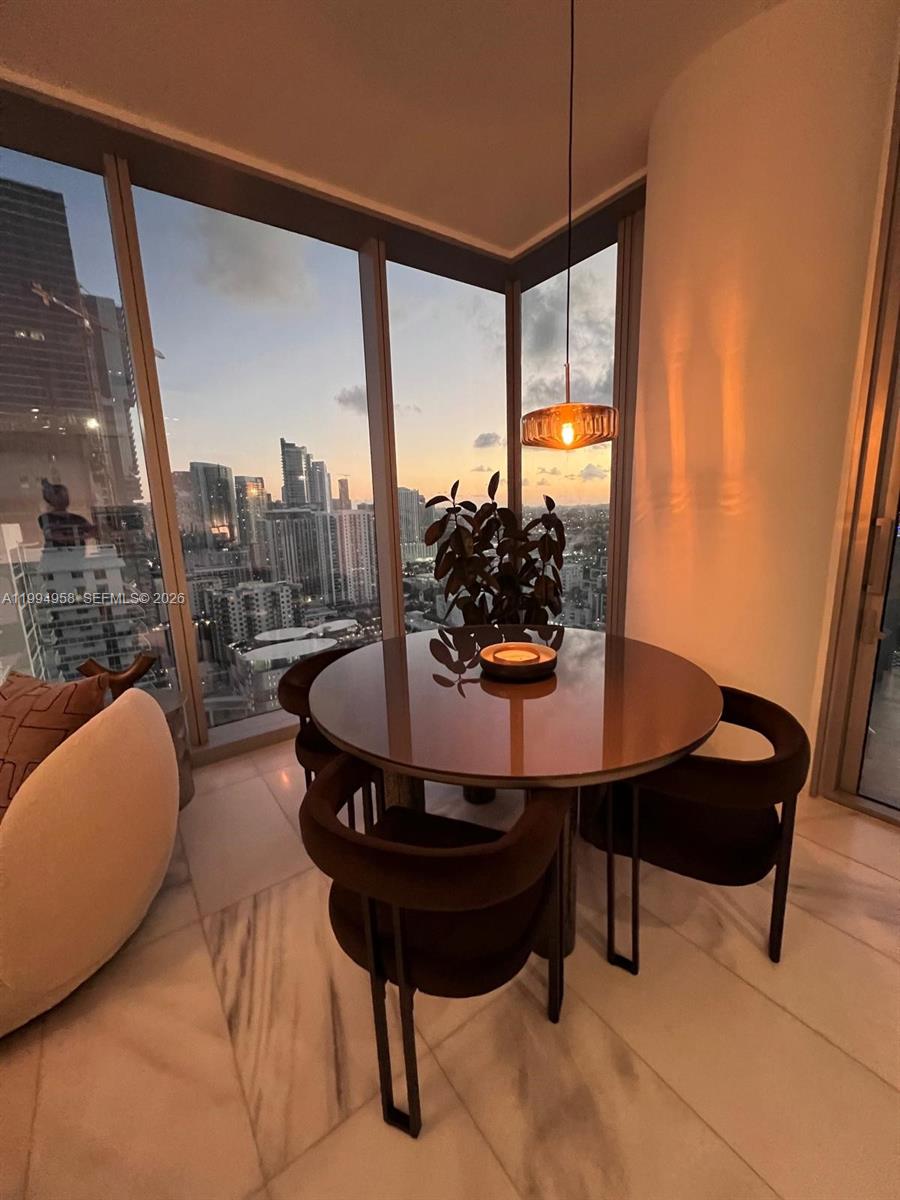 A dining area with a round table and chairs sits before floor-to-ceiling windows overlooking cityscapes — 700 NE 26th Ter # 2805, Miami FL 33137, MIAMI, FL