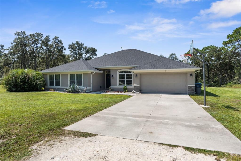 A single-story house with a gray exterior, a two-car garage, and a large front lawn — 18209 MERWYN CIR, WEEKI WACHEE, FL
