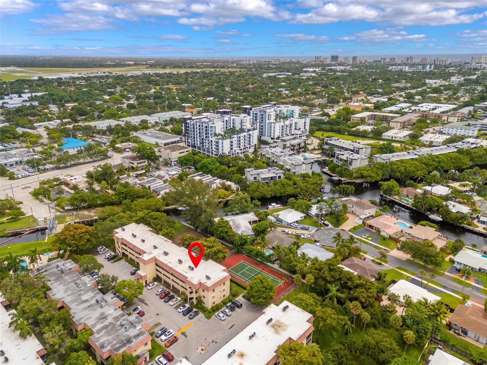 A tennis court with a chain-link fence sits in front of a grassy area and trees — 128 S Cypress Road # 827, Pompano Beach FL 33060, POMPANO BEACH, FL