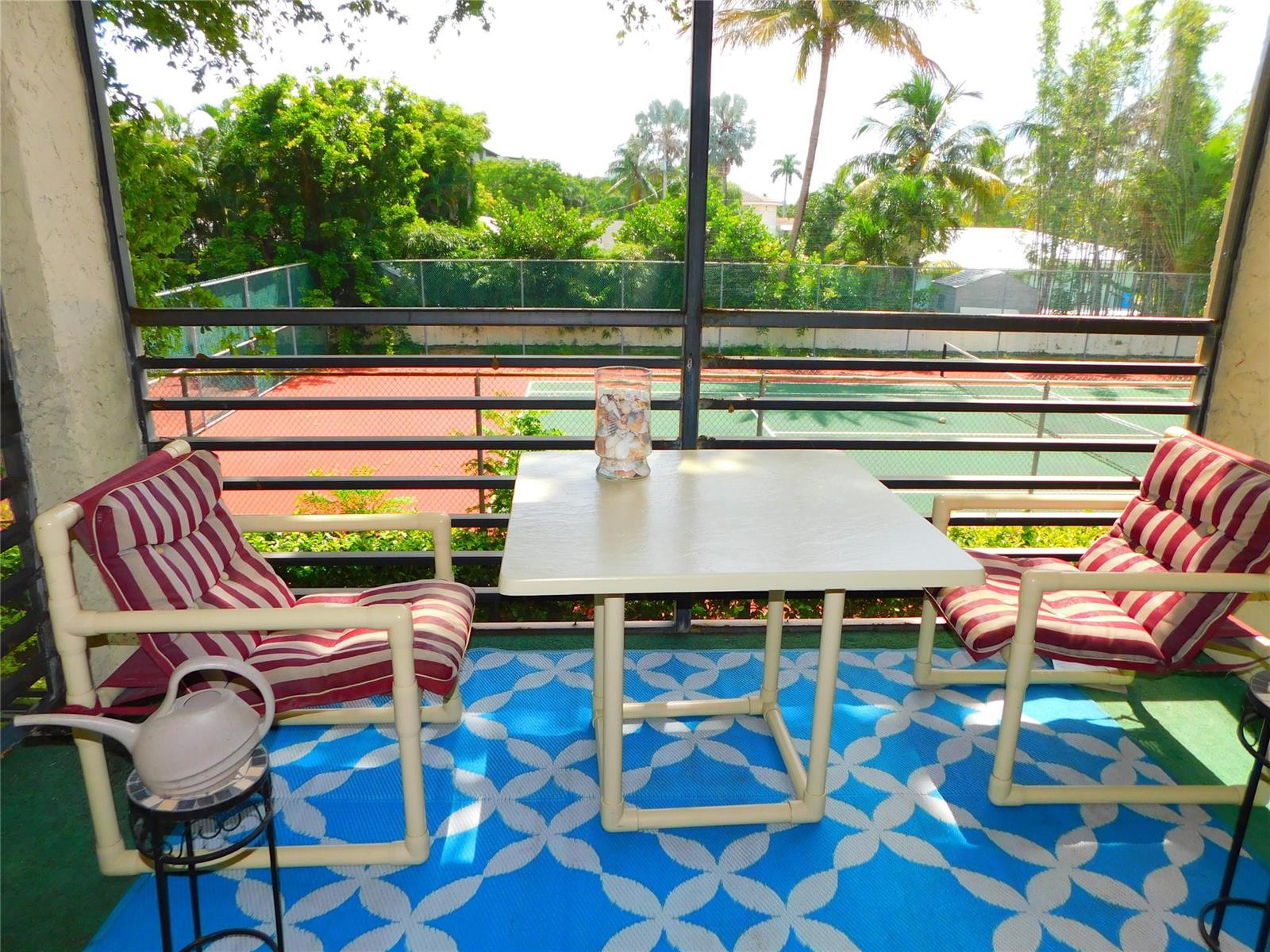 A balcony with green flooring overlooks a tennis court through a sliding glass door — 128 S Cypress Road # 827, Pompano Beach FL 33060, POMPANO BEACH, FL