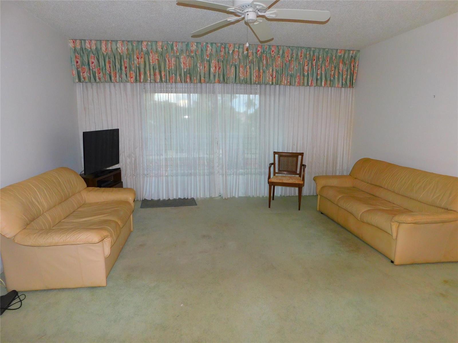 An empty living room features green wall-to-wall carpeting, a vintage amber chandelier, and a sliding door — 128 S Cypress Road # 827, Pompano Beach FL 33060, POMPANO BEACH, FL