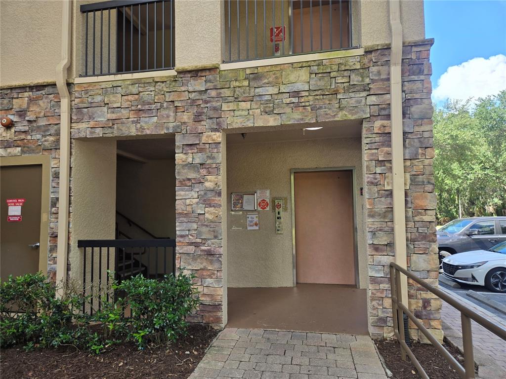 The exterior entrance of a building features stone veneer siding, a metal door, and stairs — 1301 TUSCAN TERRACE UNIT 9408, DAVENPORT, FL