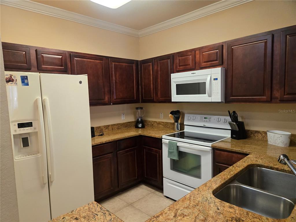 A kitchen features dark wood cabinets, granite countertops, and white appliances — 1301 TUSCAN TERRACE UNIT 9408, DAVENPORT, FL