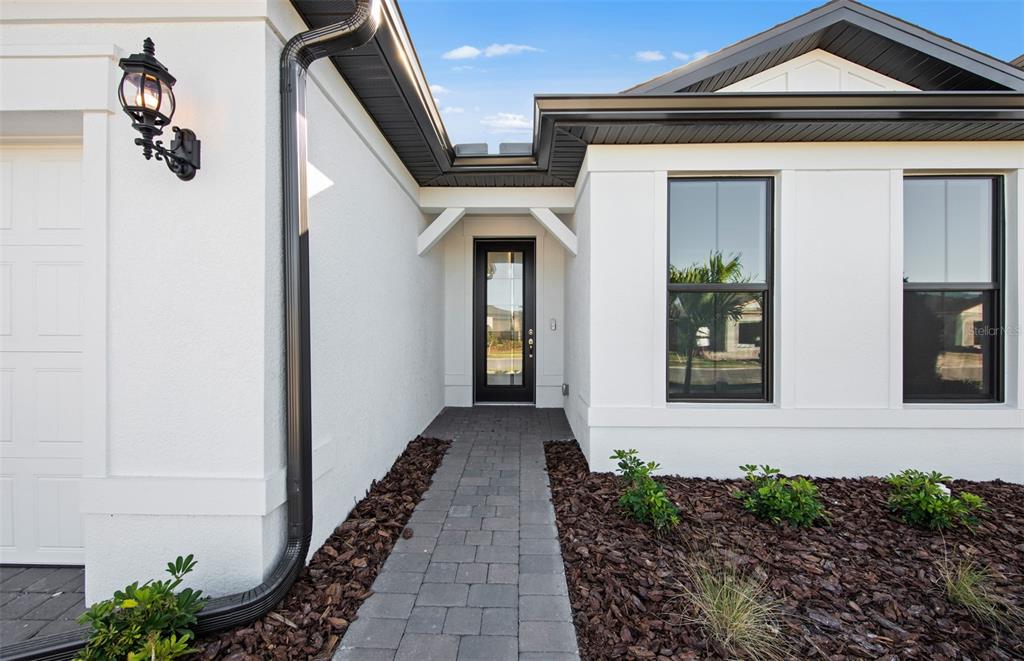 A paved walkway leads to the front entrance of a white house with black trim — 2657 GABEL OAK DRIVE, NORTH PORT, FL
