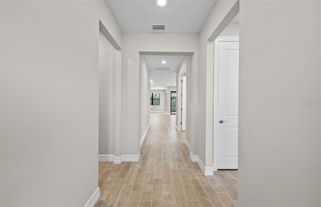 A hallway with light-colored walls and wood-look tile flooring leads toward an open living area — 2657 GABEL OAK DRIVE, NORTH PORT, FL