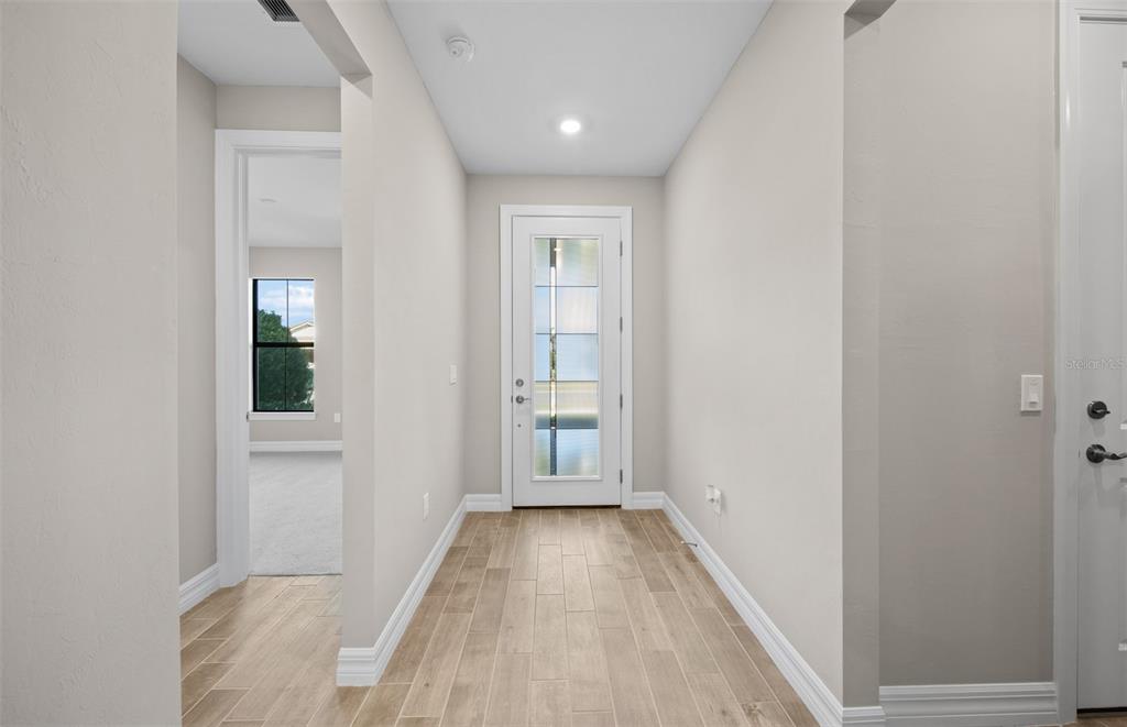 A hallway with light wood-look tile flooring leads to a glass-paneled exterior door — 2657 GABEL OAK DRIVE, NORTH PORT, FL
