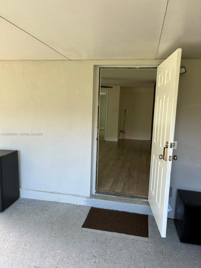 A white door opens from a speckled concrete garage into a room with wood flooring — 3700 NE 13th Ter # 1, Pompano Beach FL 33064, POMPANO BEACH, FL
