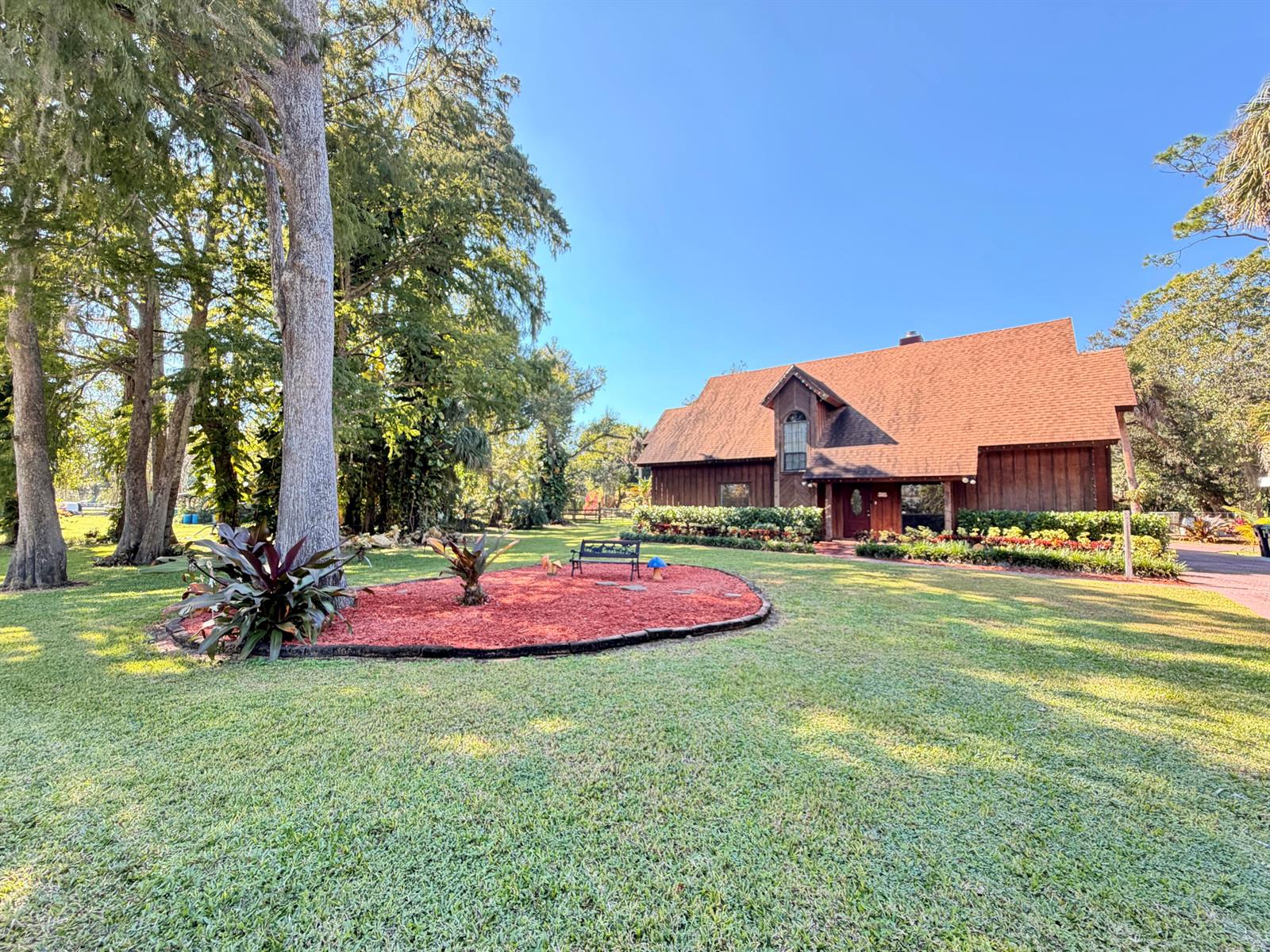 A wooden house with a steep roof sits behind a landscaped yard with red mulch — 505 SE 18th Way, Okeechobee FL 34974, OKEECHOBEE, FL
