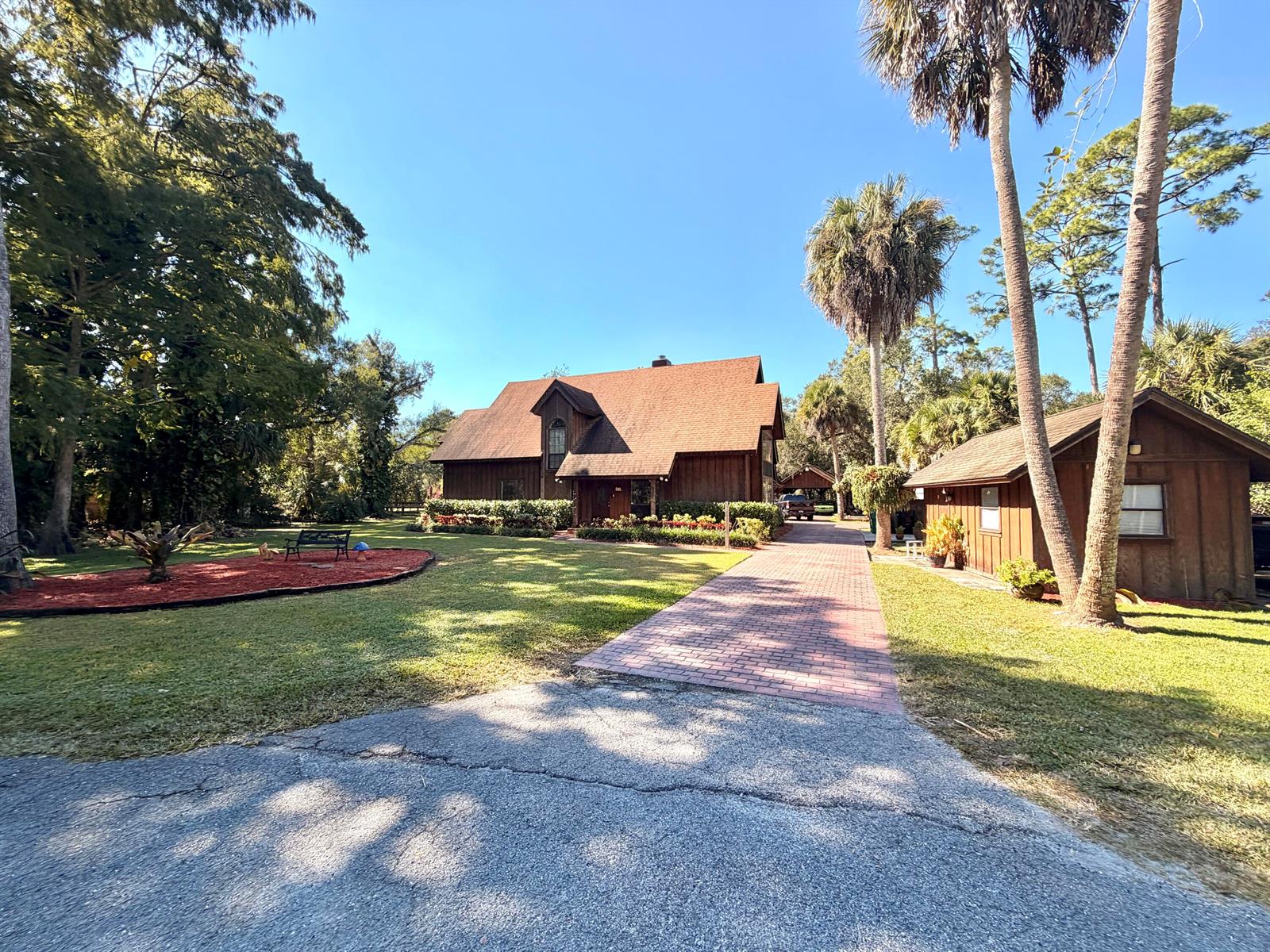 A brown wood-sided house with a brick driveway and palm trees under a clear sky — 505 SE 18th Way, Okeechobee FL 34974, OKEECHOBEE, FL