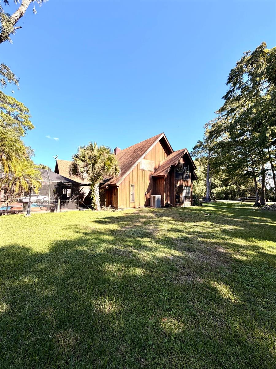 A wooden house with a steep roof and a screened-in pool area sits on grass — 505 SE 18th Way, Okeechobee FL 34974, OKEECHOBEE, FL