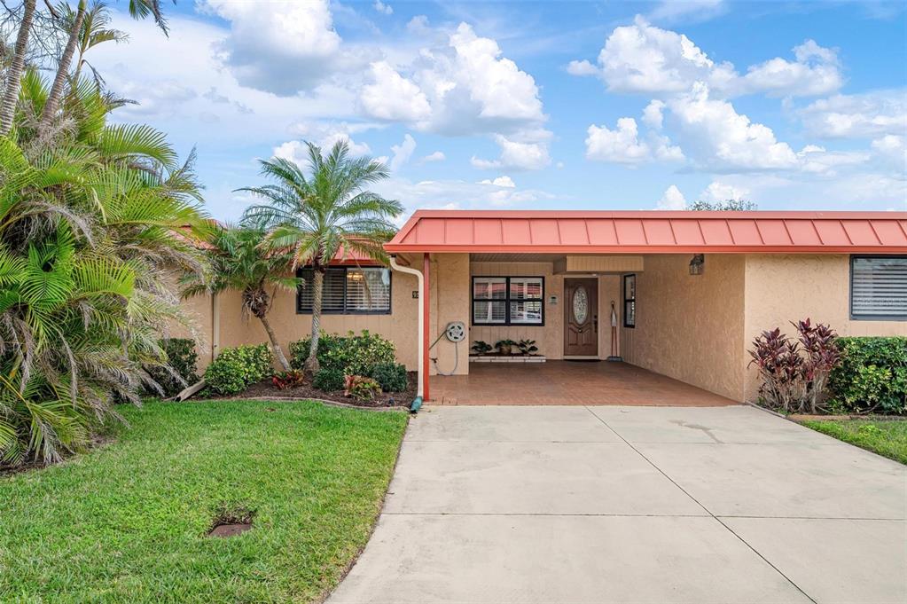A single-story house with a tan stucco exterior, a red metal roof, and a driveway — 9527 AZURE COVE, BRADENTON, FL