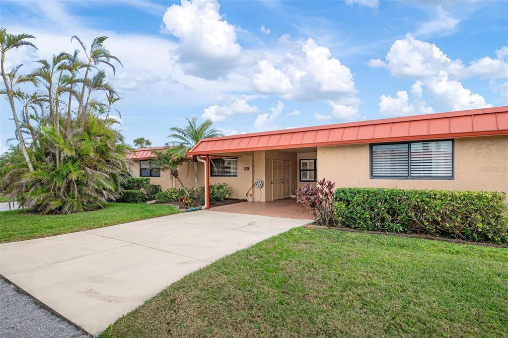 A single-story house with a tan stucco exterior, a red metal roof, and a carport — 9527 AZURE COVE, BRADENTON, FL