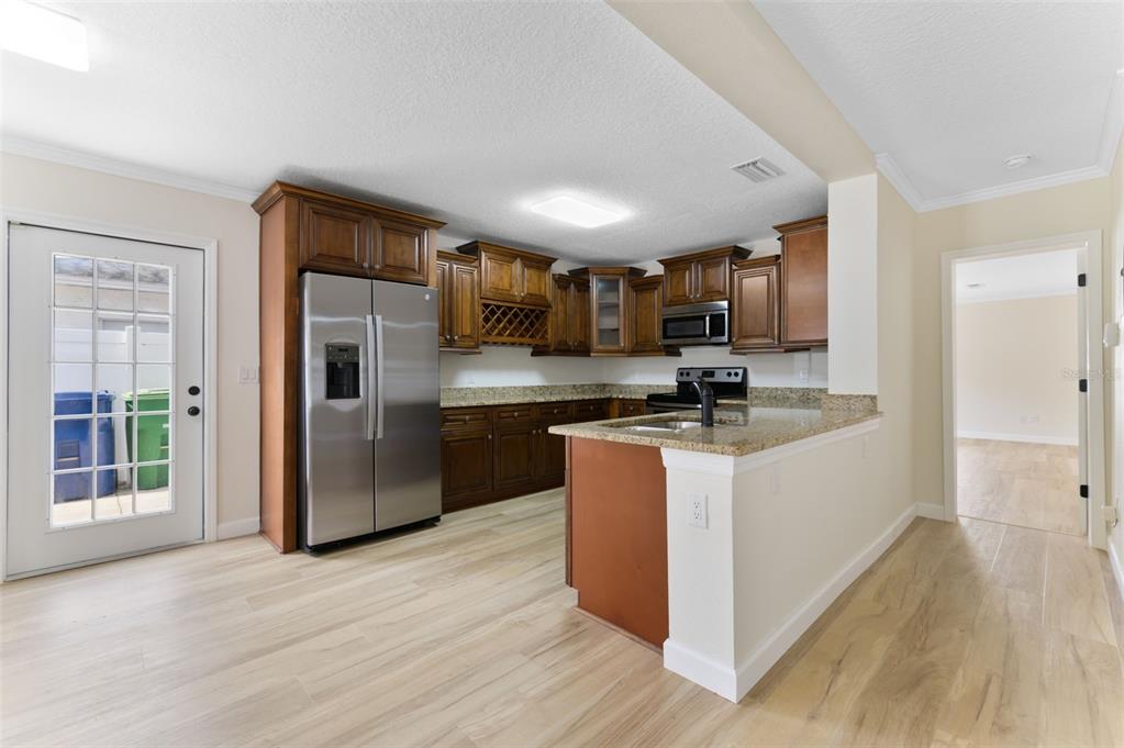 A kitchen with wood cabinets, granite countertops, stainless steel appliances, and light wood-look flooring — 4727 W BAY VISTA AVENUE, TAMPA, FL