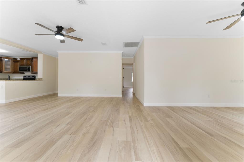 An open-concept living area features light wood-look flooring, beige walls, and two ceiling fans — 4727 W BAY VISTA AVENUE, TAMPA, FL